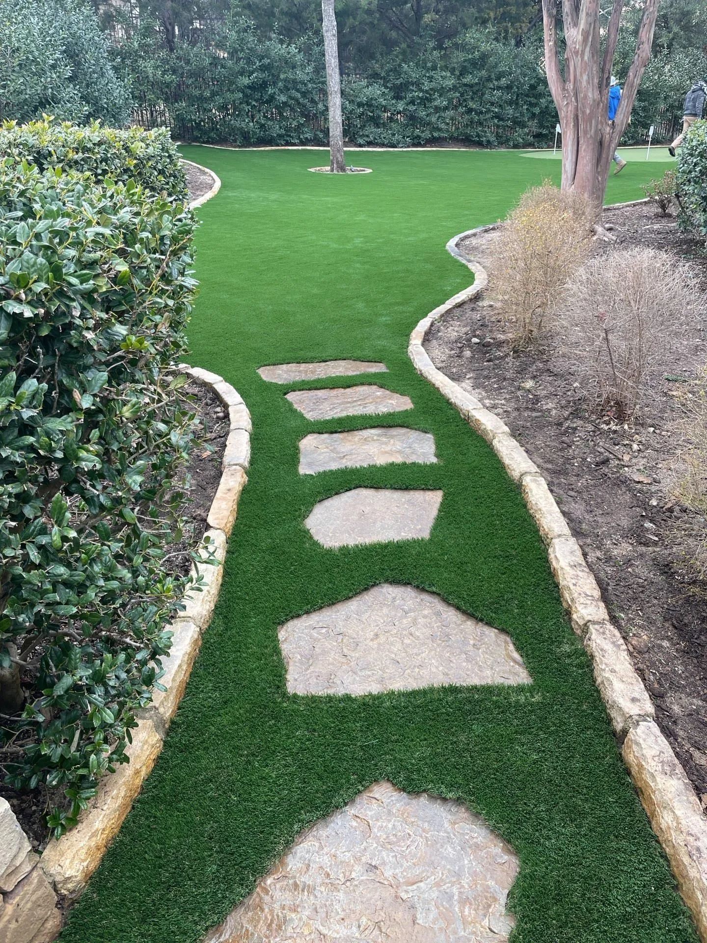 Stepping stones through a green lawn path bordered by shrubs and dry grasses