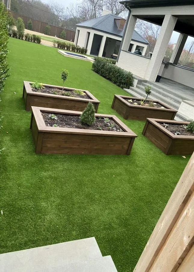 Backyard patio with artificial grass and several wooden planter boxes near a house