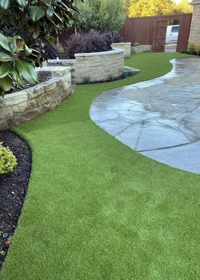 Curved green lawn beside a stone retaining wall and paved patio in a landscaped backyard