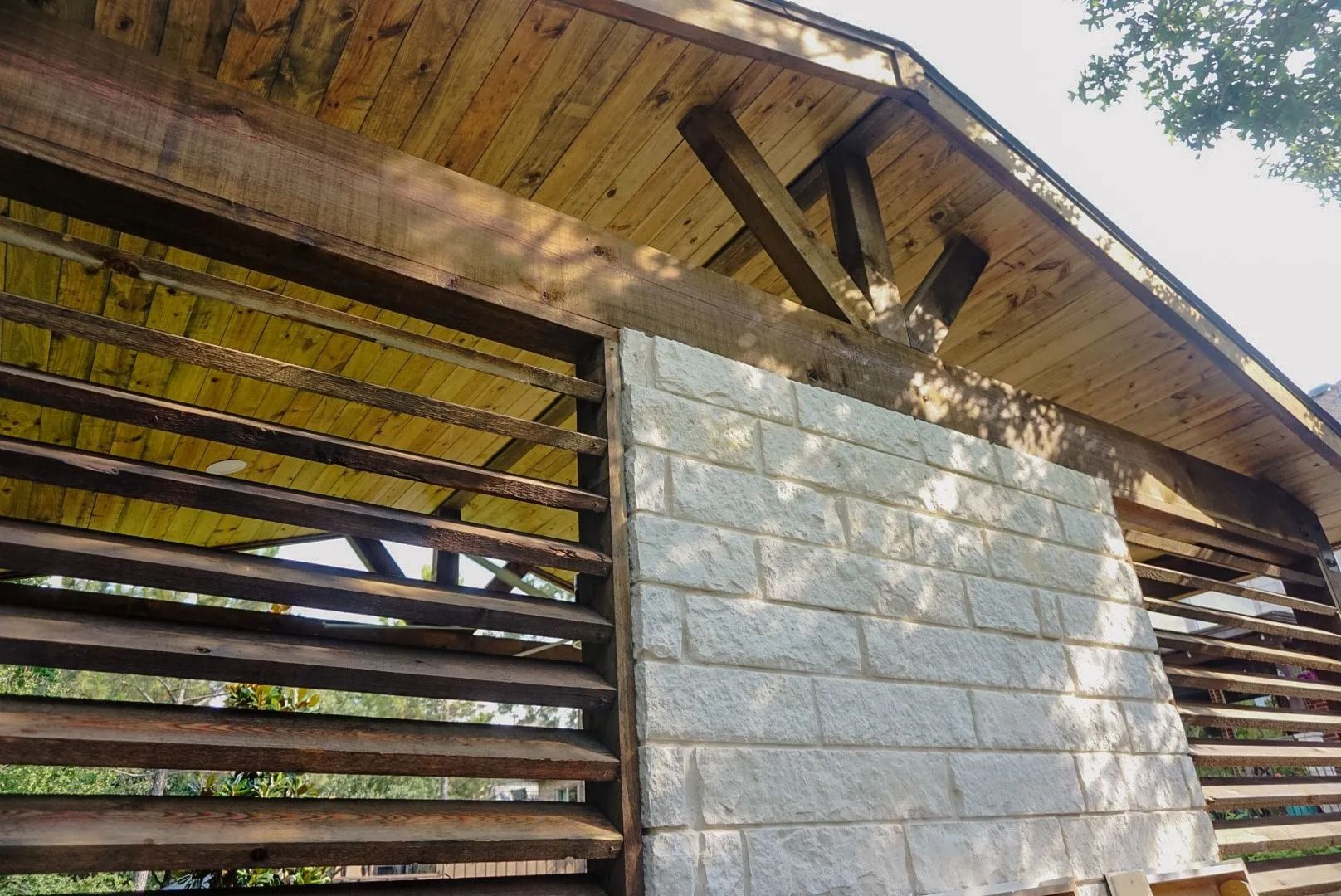 Rustic wooden and cinder block shed wall with slatted openings under a weathered roof.