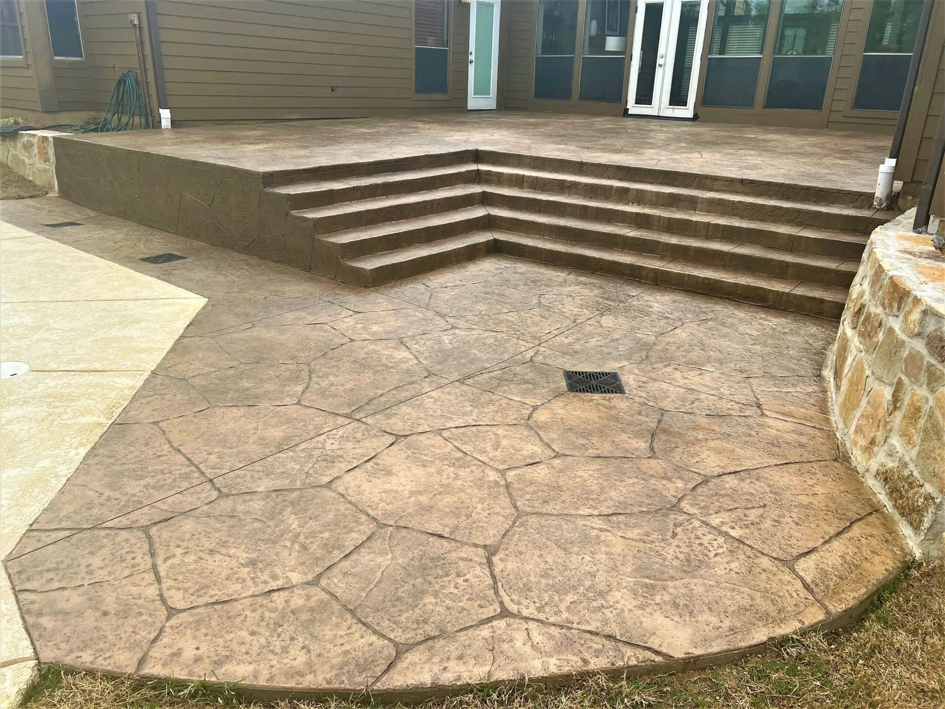 Concrete courtyard with cracked stamped paving and steps leading to a building entrance
