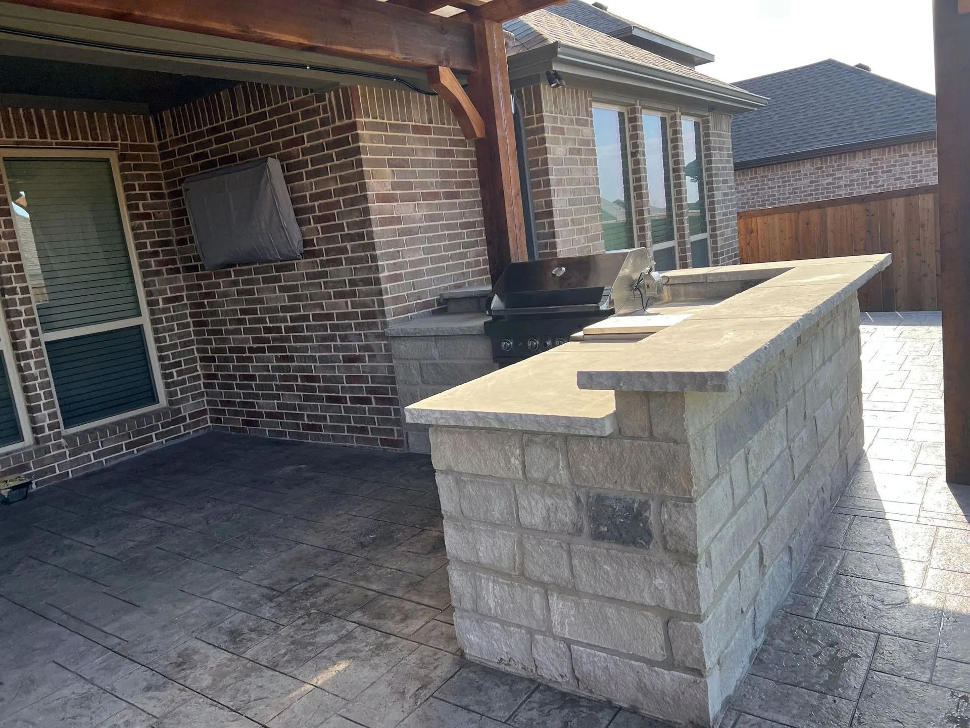 Covered brick patio with a built-in stone bar and outdoor sink beside a house
