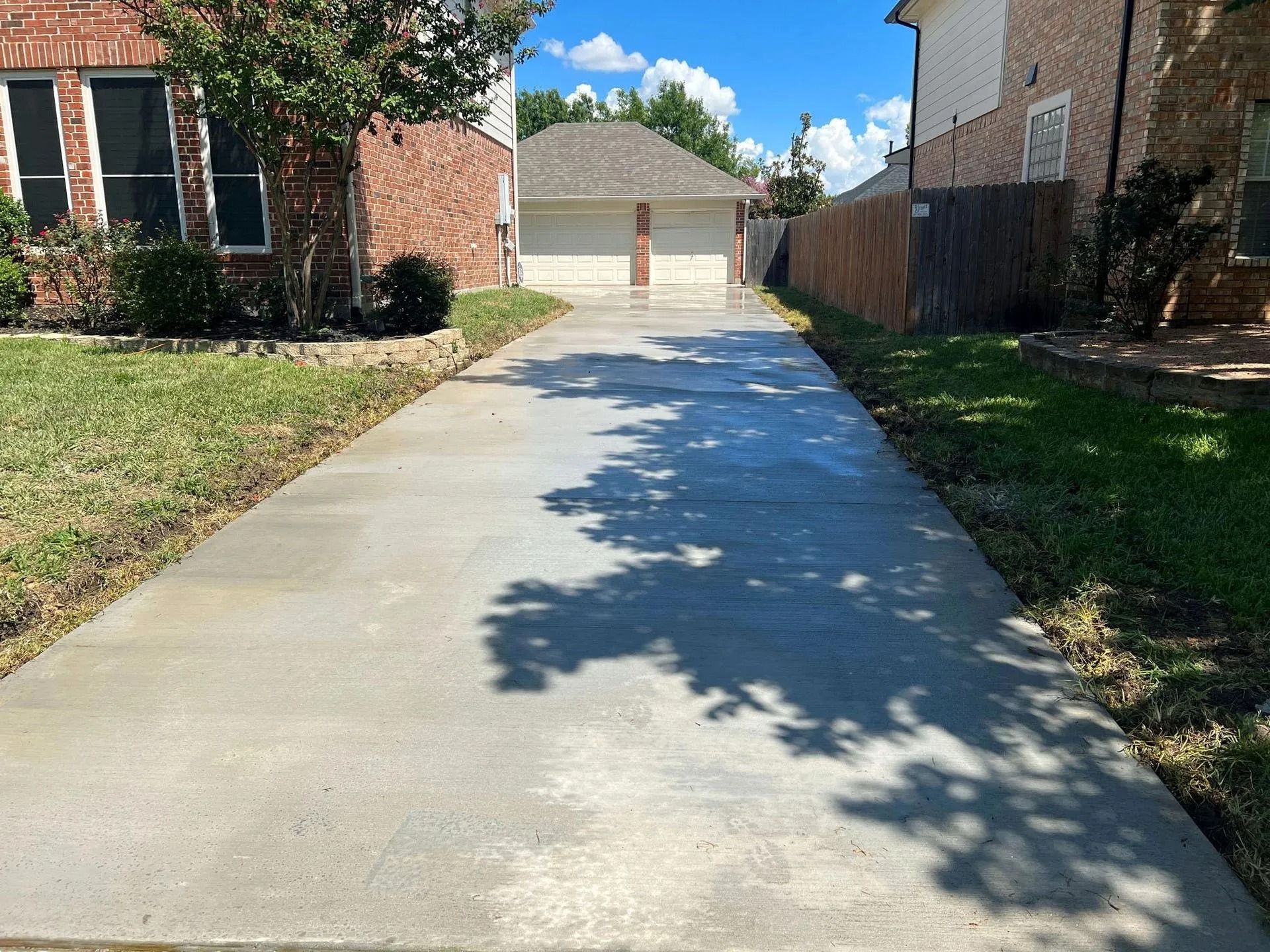 Concrete driveway leading to a detached garage between brick houses on a sunny day
