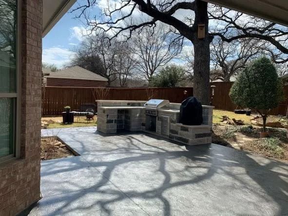 Backyard patio with stone grill island, concrete patio, and leafless trees casting shadows