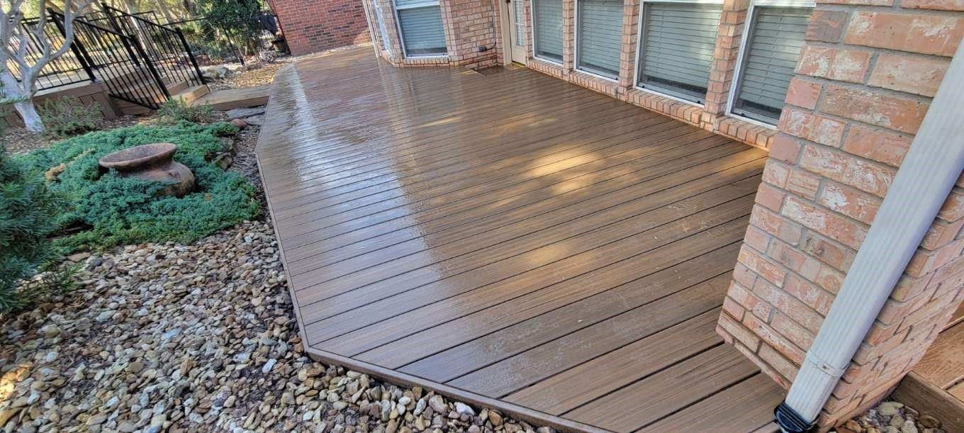 Wet wooden deck beside a brick house with sliding glass doors and garden beds on the left
