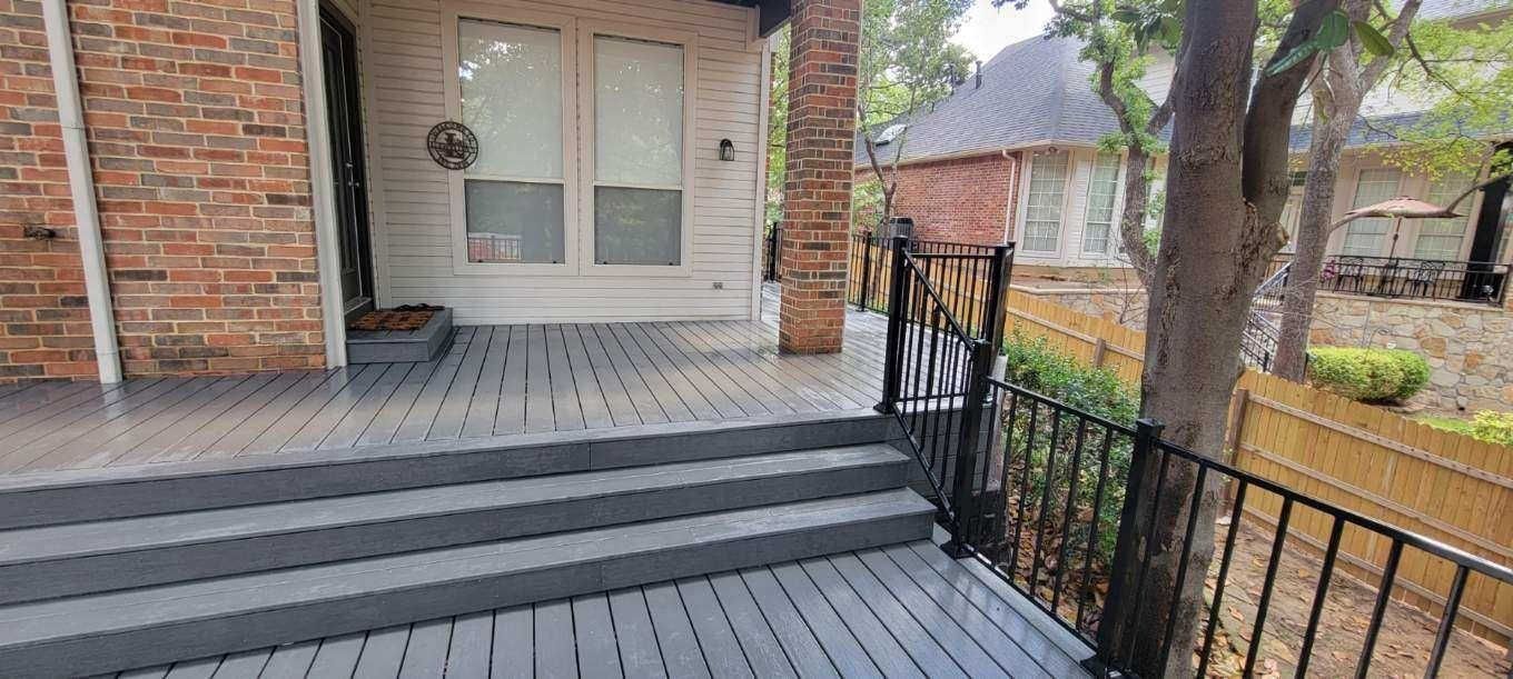 Front porch with gray steps, black railing, and white front door on a brick house
