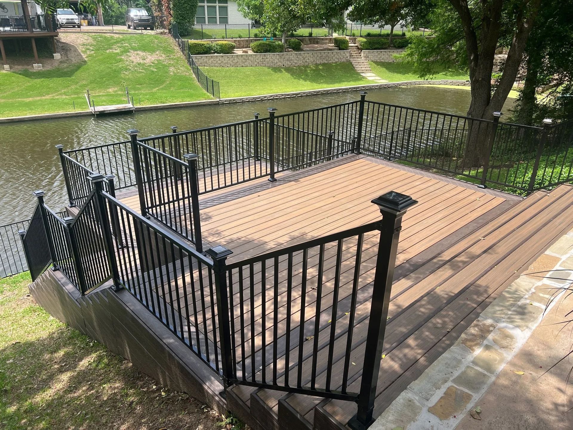 Black metal-railed wooden deck overlooking a grassy canal