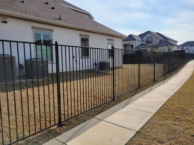 Black metal fence along a concrete sidewalk beside a suburban house and dry yard
