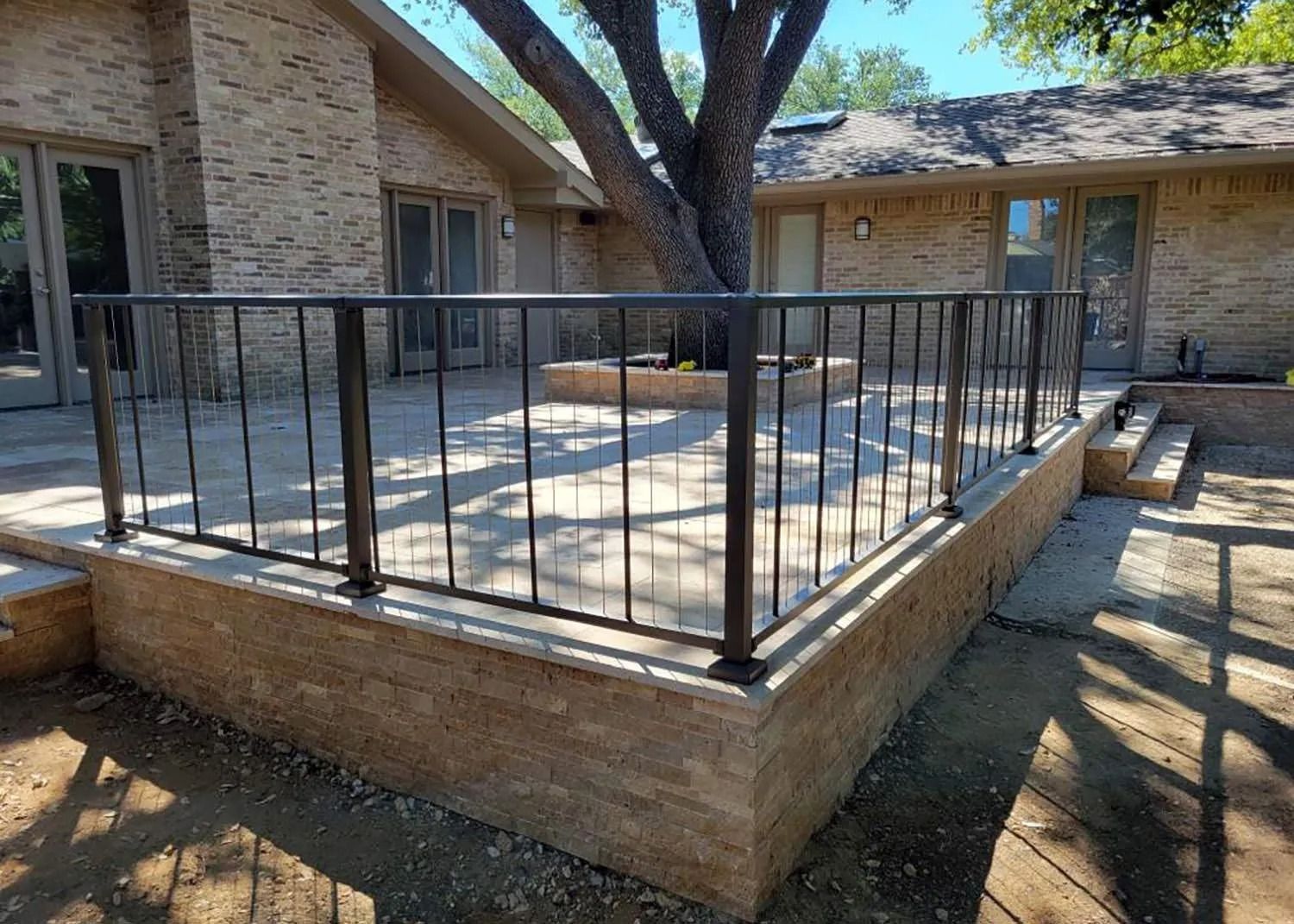 Raised concrete patio with black metal railing in a courtyard under trees
