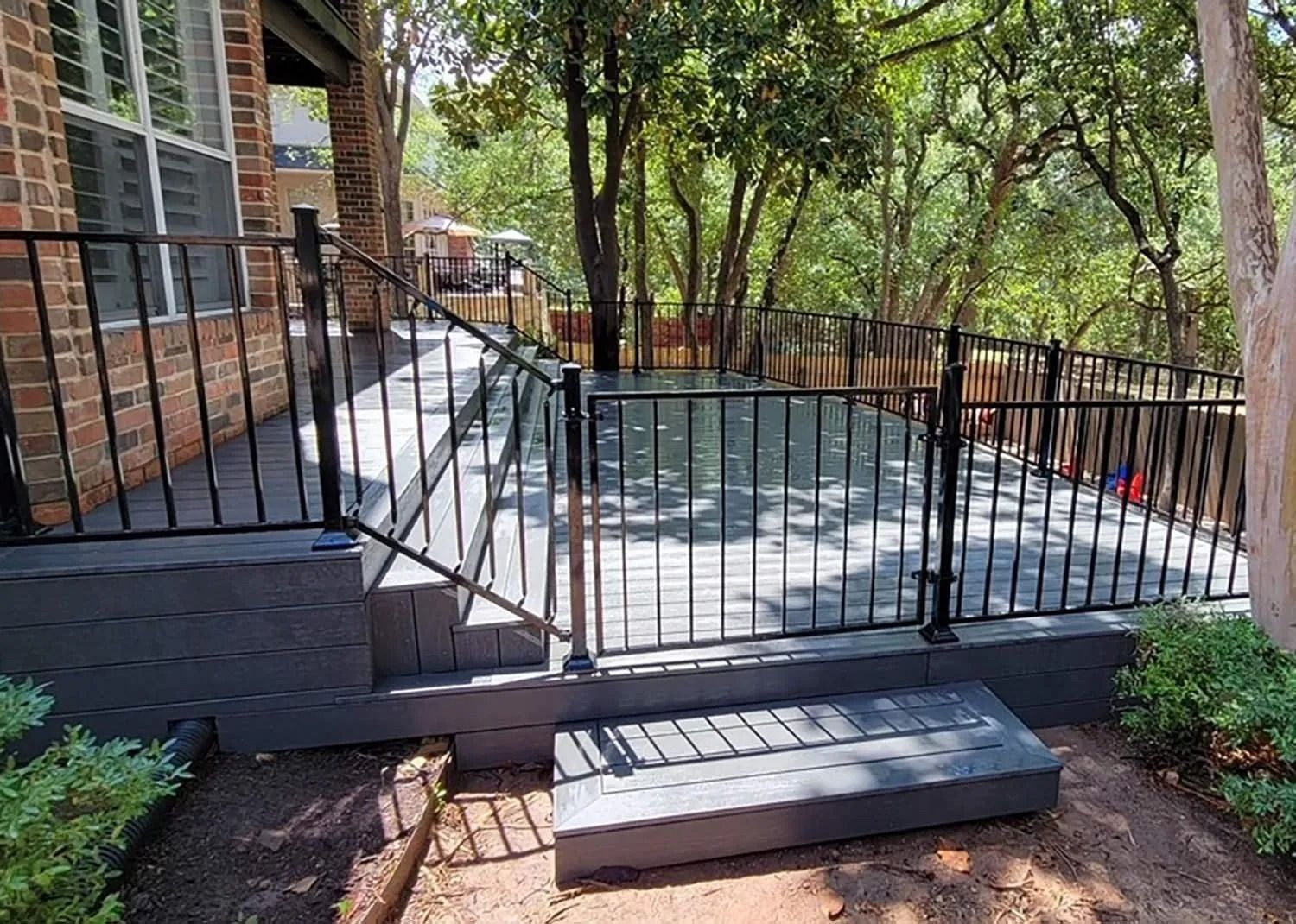 Backyard patio with metal railing, short steps, and trees in the background

