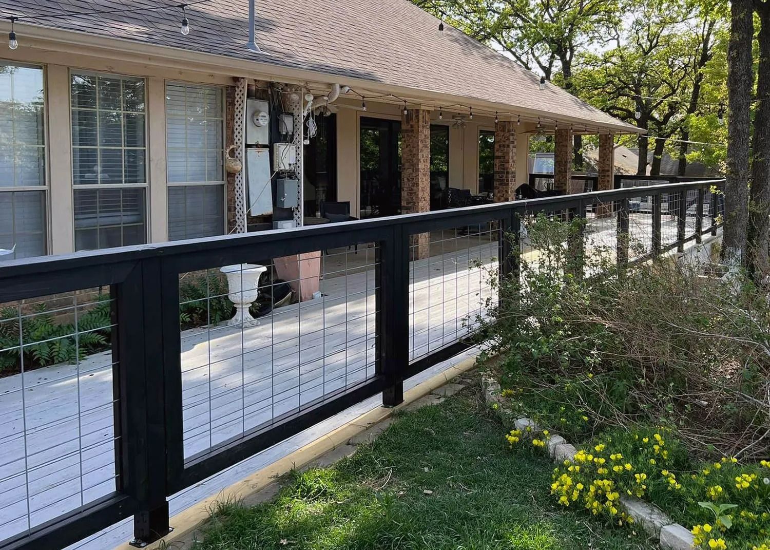 Black metal fence along a brick house with a porch and landscaped front yard
