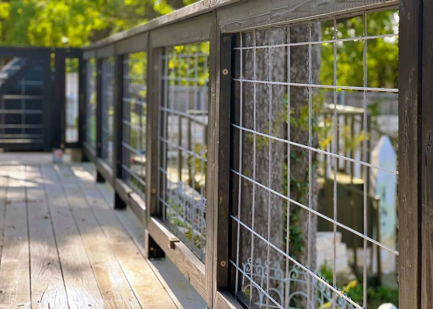 Wooden walkway with black railing and wire mesh overlooking greenery
