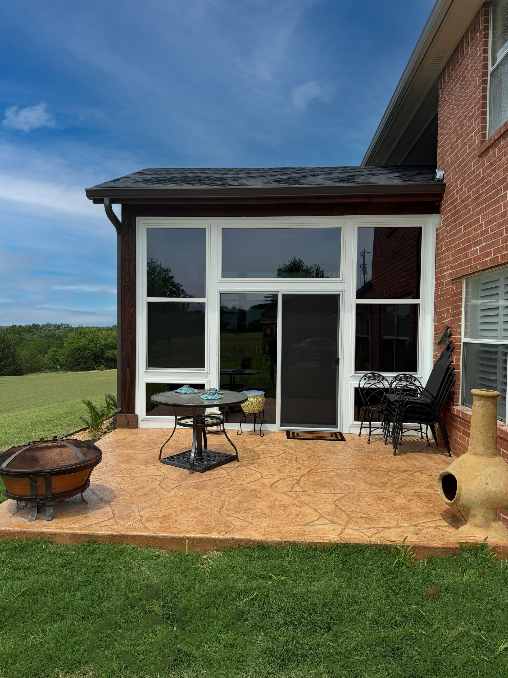 Patio with white sunroom, sliding glass doors, wicker table, and brick house beside a grassy lawn.