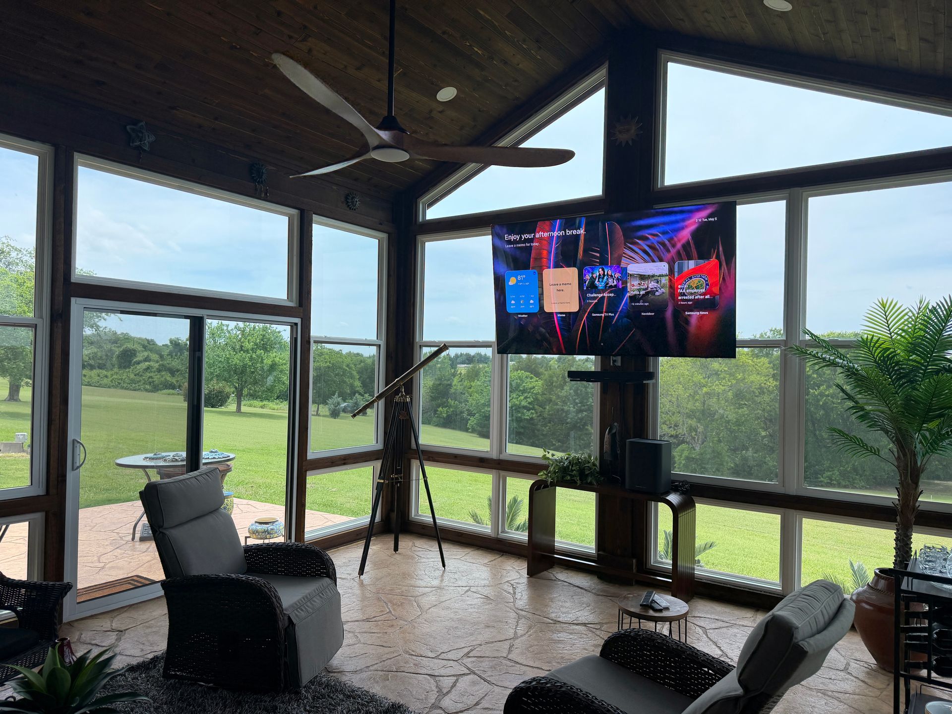Screened porch with TV, chairs, and ceiling fan overlooking a grassy yard