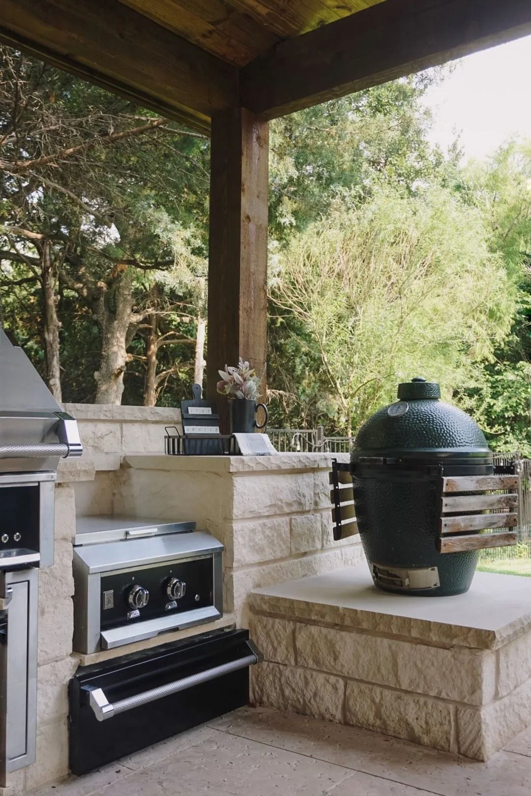 Outdoor patio with a built-in grill, stone counter, and green ceramic smoker under a covered roof