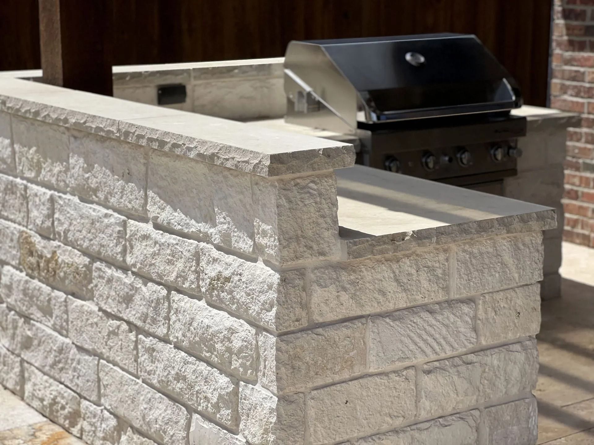 Stone outdoor grill beside a tan masonry privacy wall in a backyard