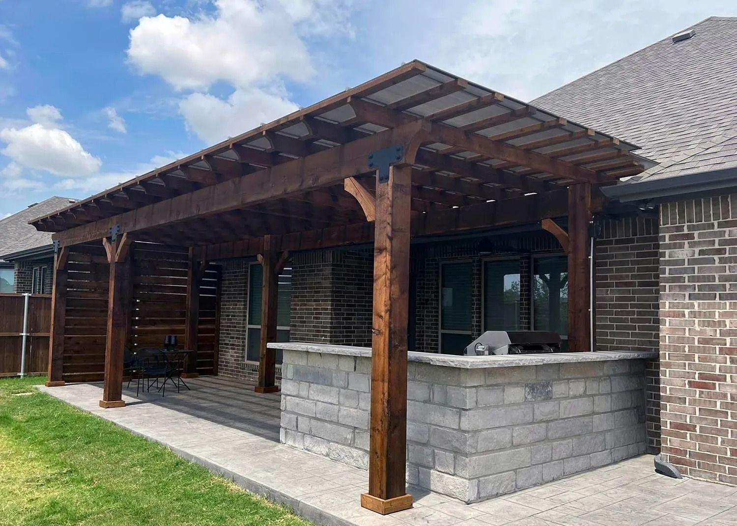 Covered patio with wooden posts and stone bar beside a brick house