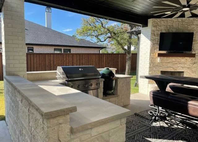 Covered outdoor patio with stone counter, grill, TV, and seating area in a backyard