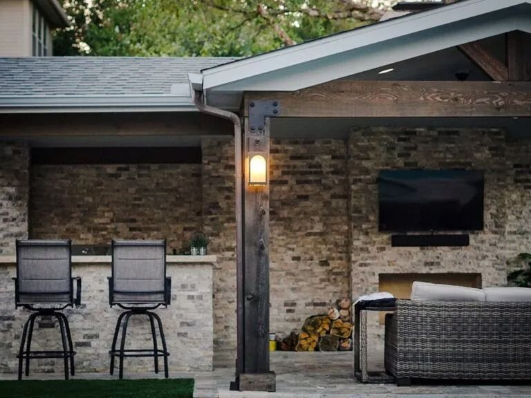 Backyard patio with brick wall, bar stools, lantern light, and wicker seating under a roofed patio