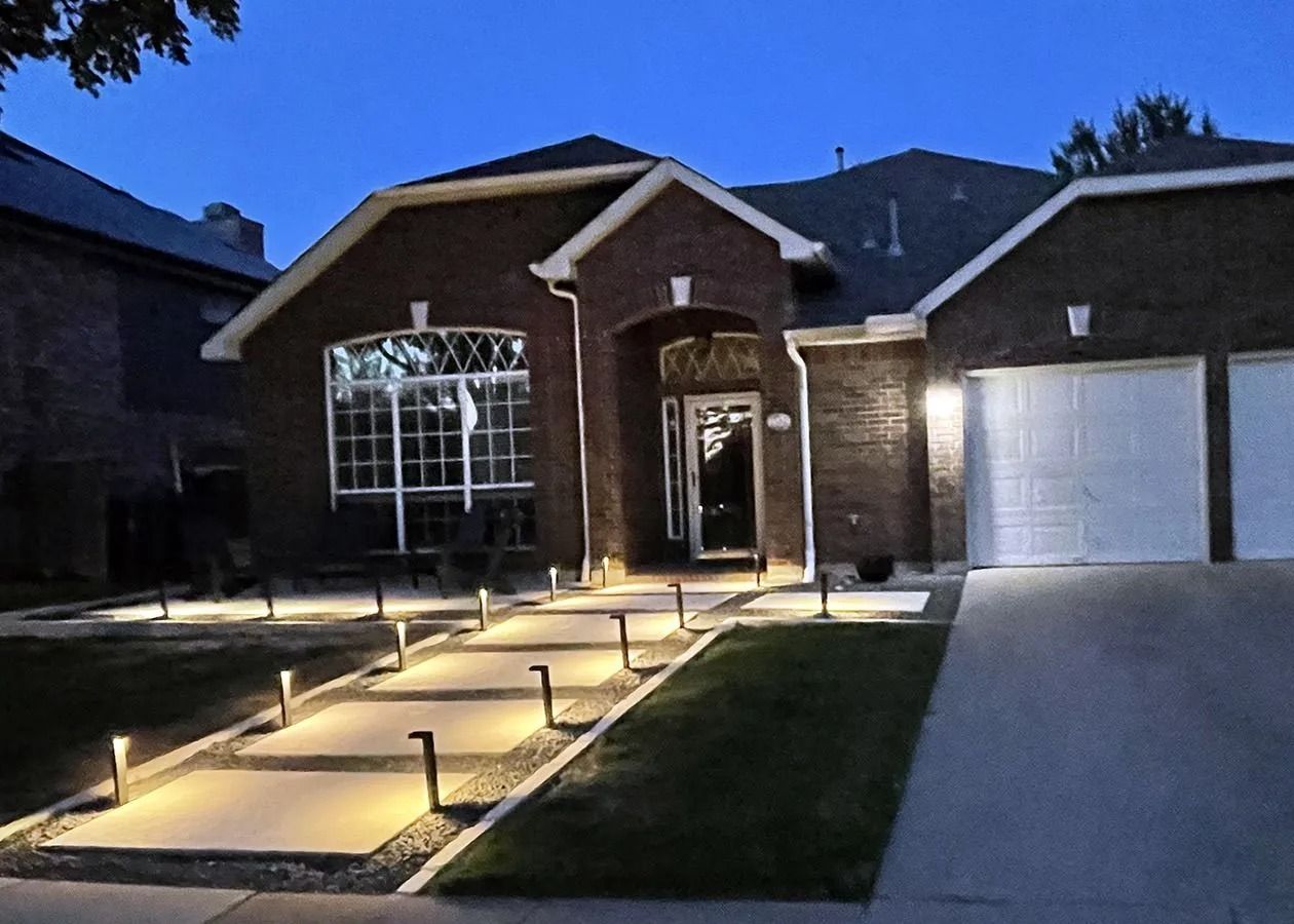 Brick house exterior at dusk with lit front walkway and two white garage doors
