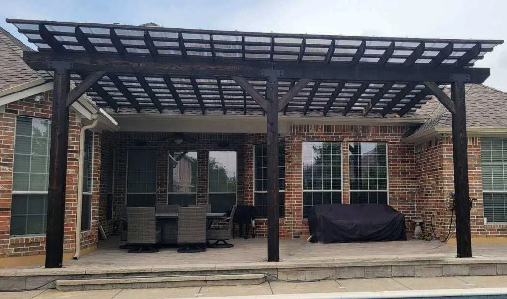 Brick patio with a wooden pergola, stacked chairs, and a covered table in front of a house