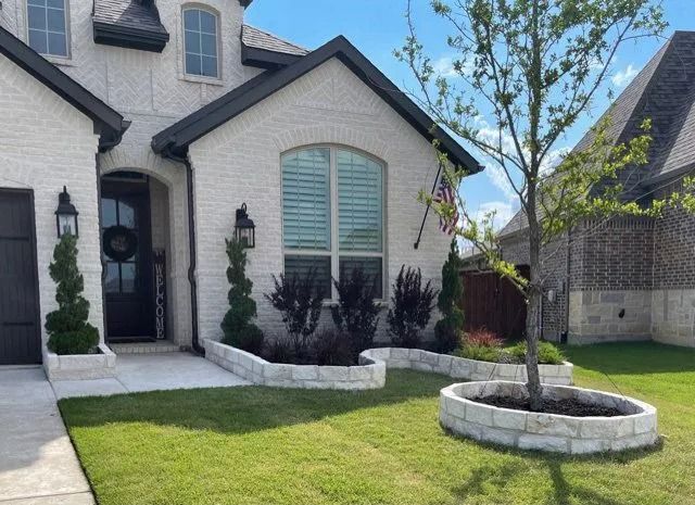 Suburban brick house with manicured lawn, black front door, and young trees in stone planters