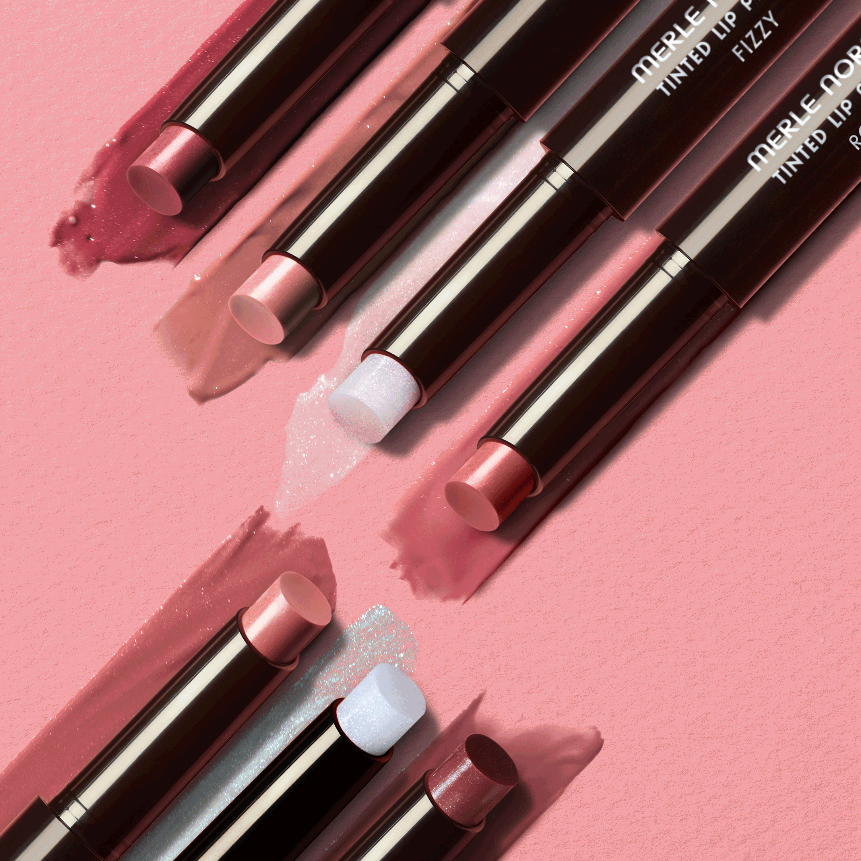 Several lip balm sticks with color swatches arranged on a soft pink surface