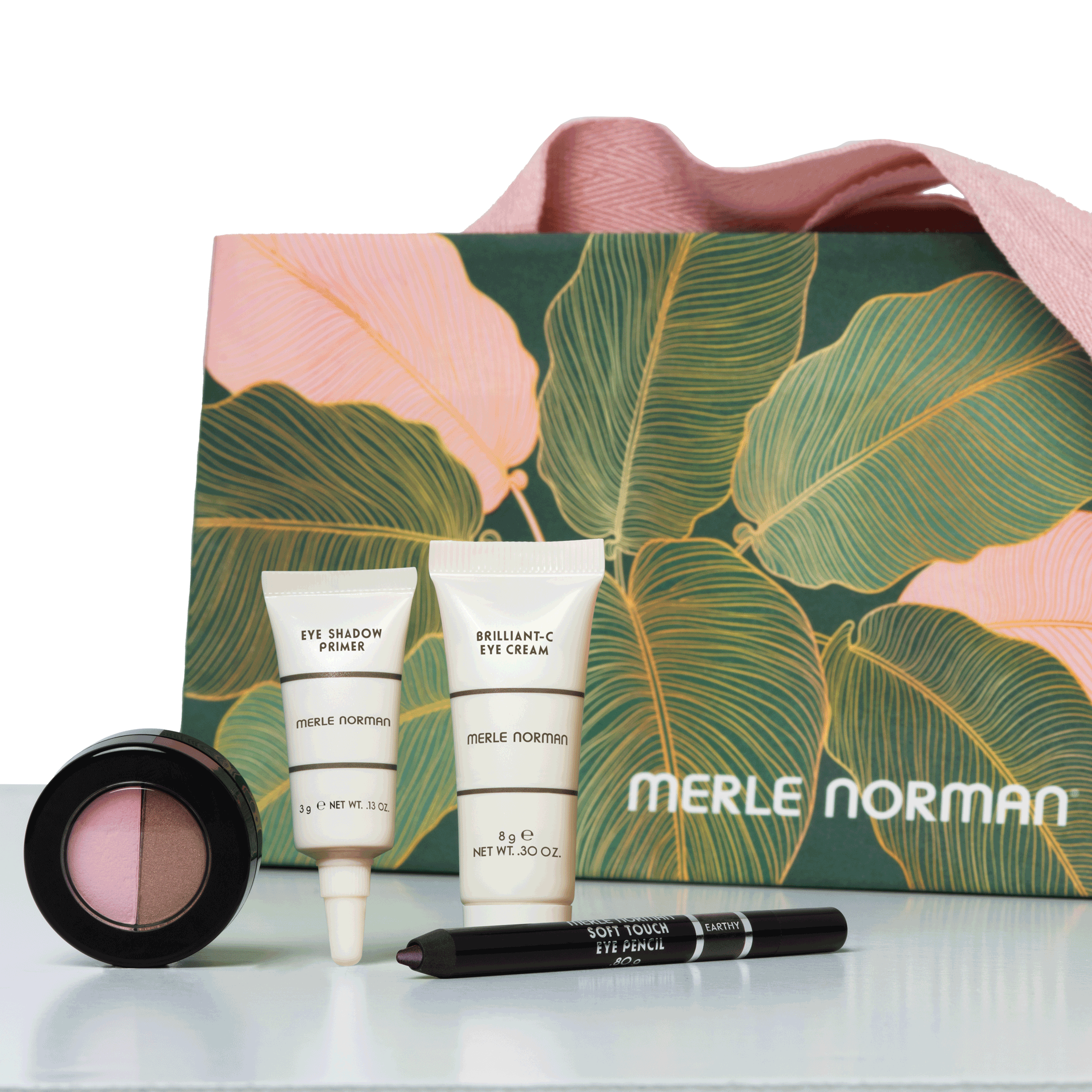 Merle Norman beauty products, including a duo eyeshadow, two tubes, and an eyeliner, set against a leafy decorative box