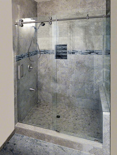 Glass shower with sliding door and built-in niche. Features gray tiles, brushed metal fixtures, and stone flooring.