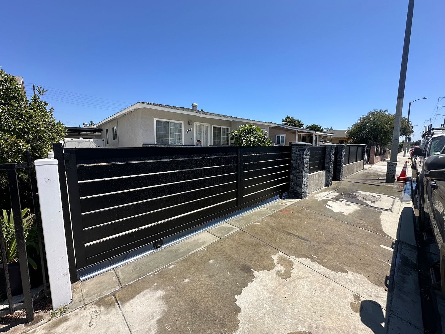 Black horizontal slat fence in front of a house on a sunny day.