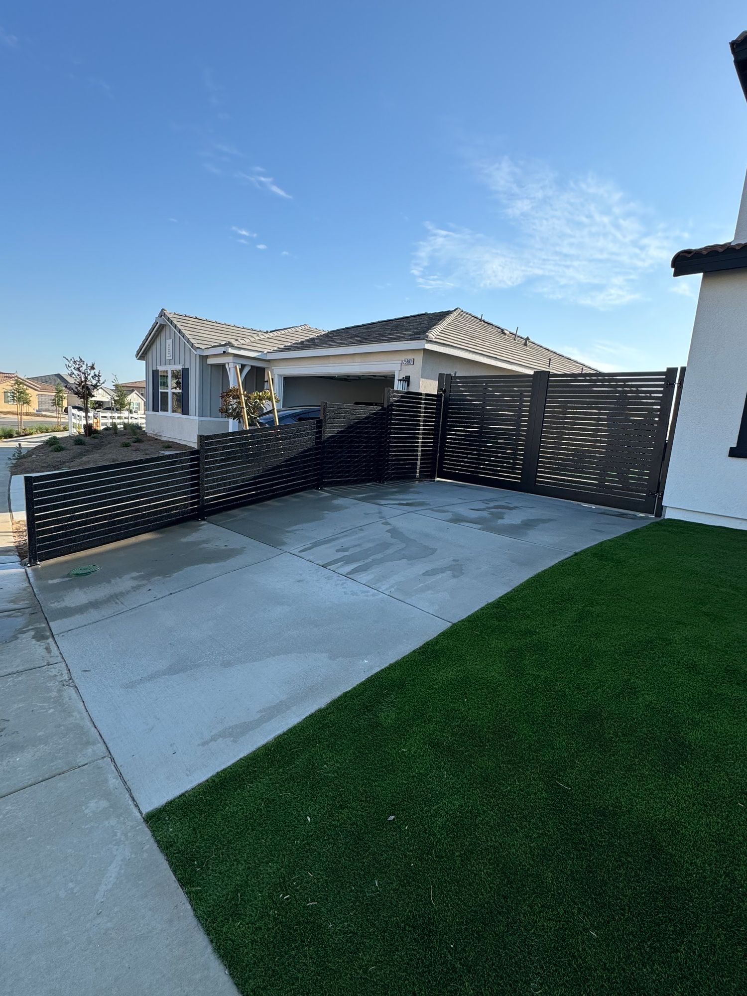 Black decorative fence surrounding a driveway, with house and blue sky in the background.