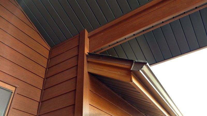 Brown wooden house exterior with siding, trim, and soffit. A gutter is attached.
