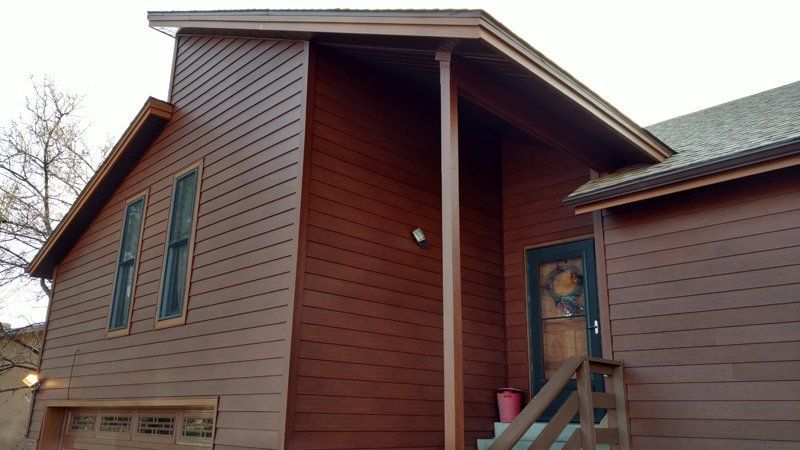 Brown-sided house with a garage, entry porch, and windows.