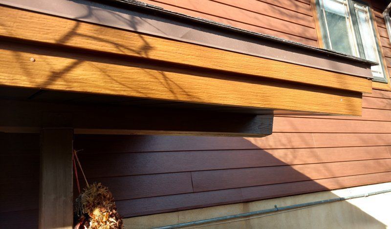 Wooden overhang on a reddish-brown house with horizontal siding; sunny, shadow cast.