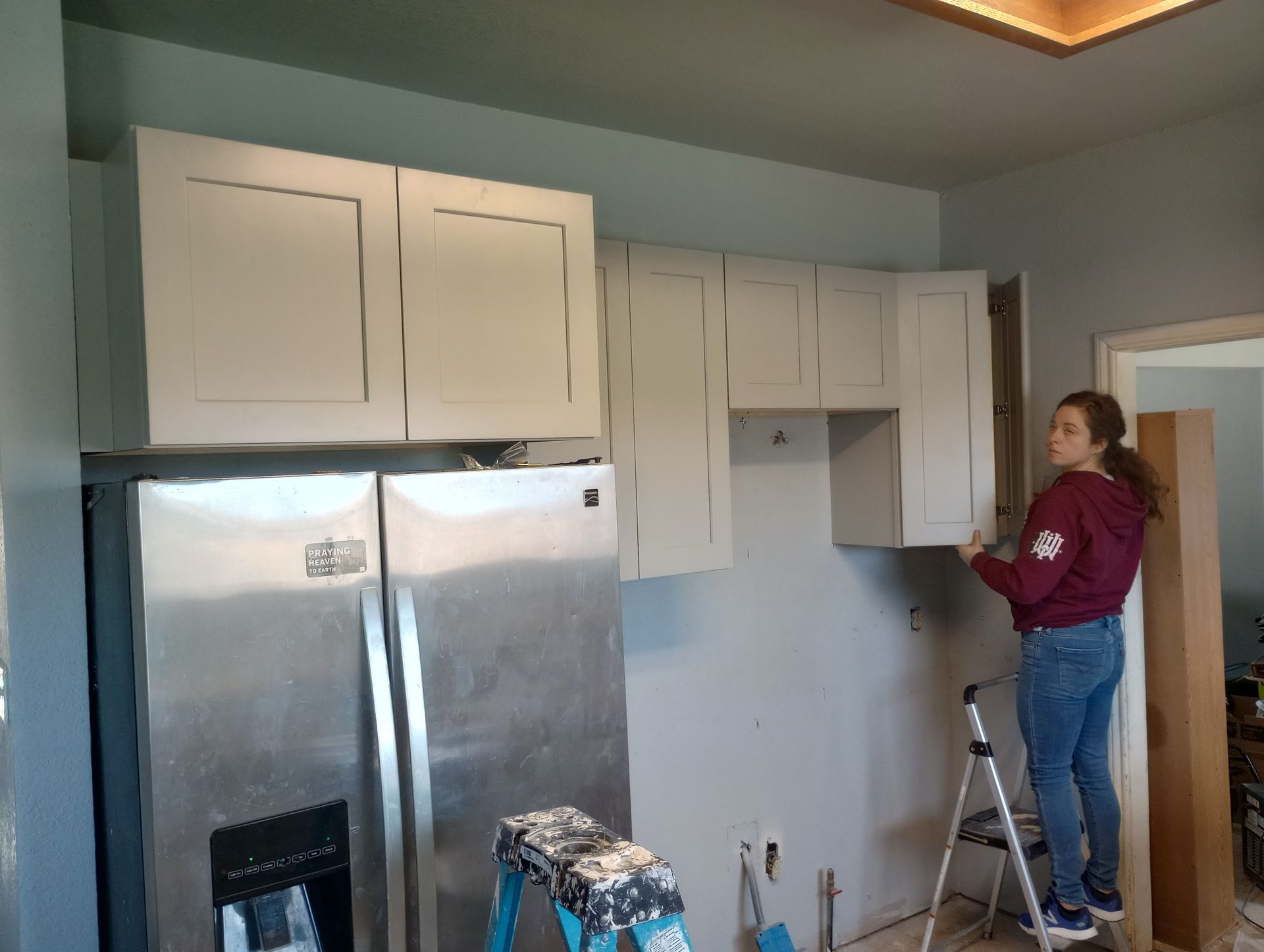 A woman is standing on a ladder in a kitchen.