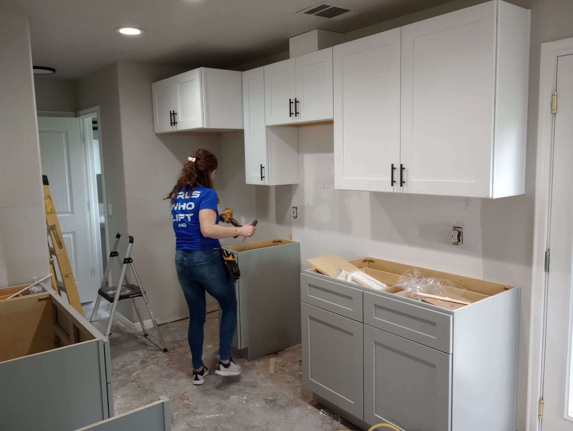 A woman in a blue shirt is working on a kitchen.