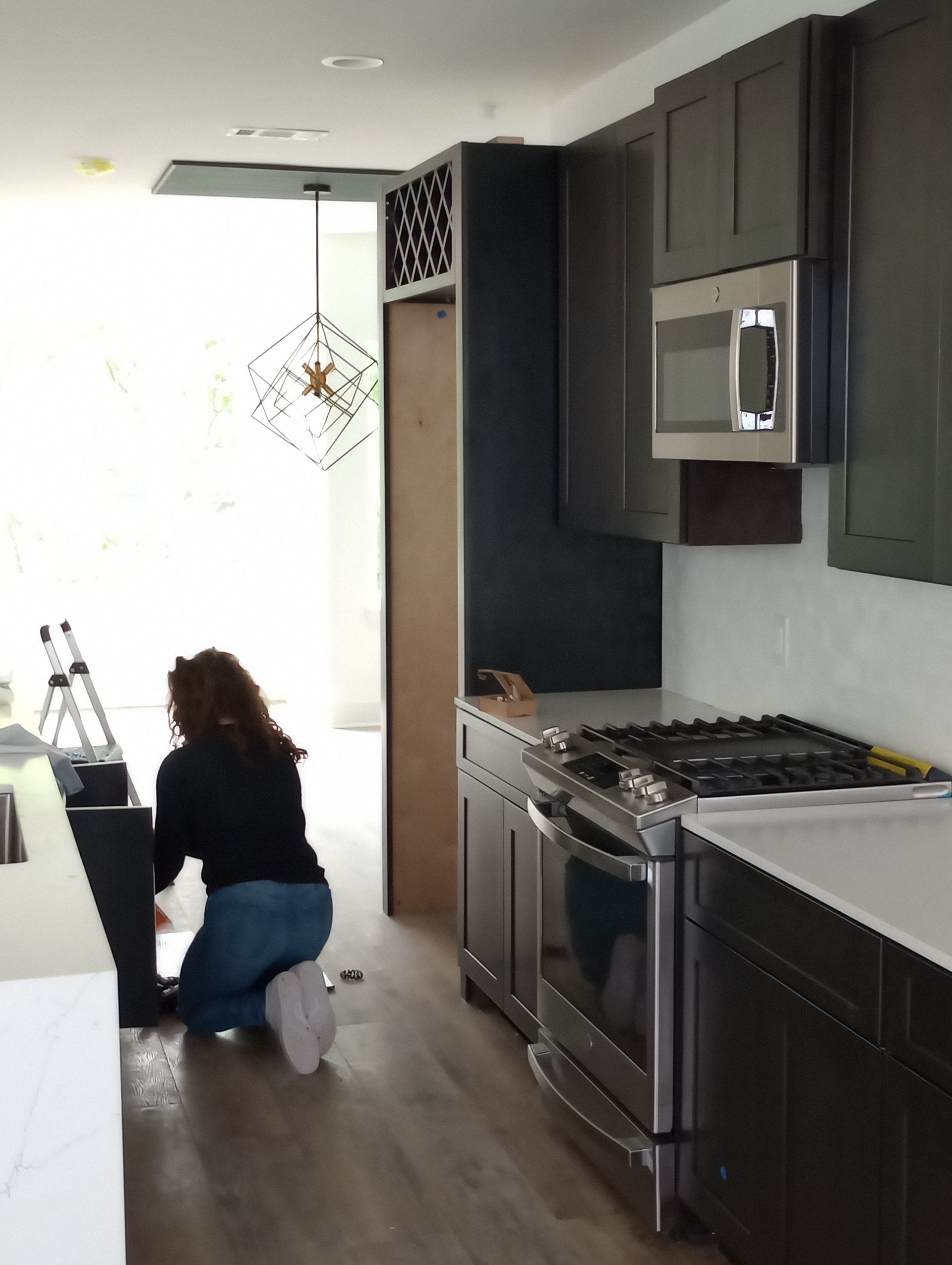 A woman is kneeling down in a kitchen near a stove.