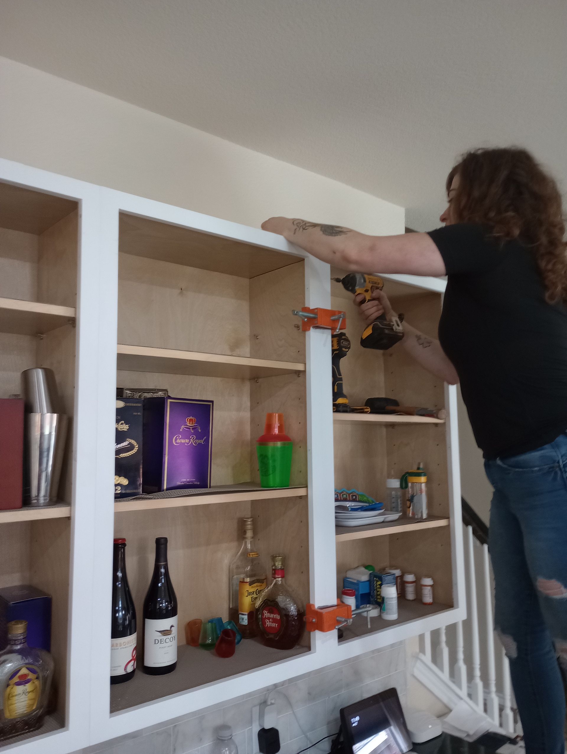 A woman is working on a shelf with bottles on it.