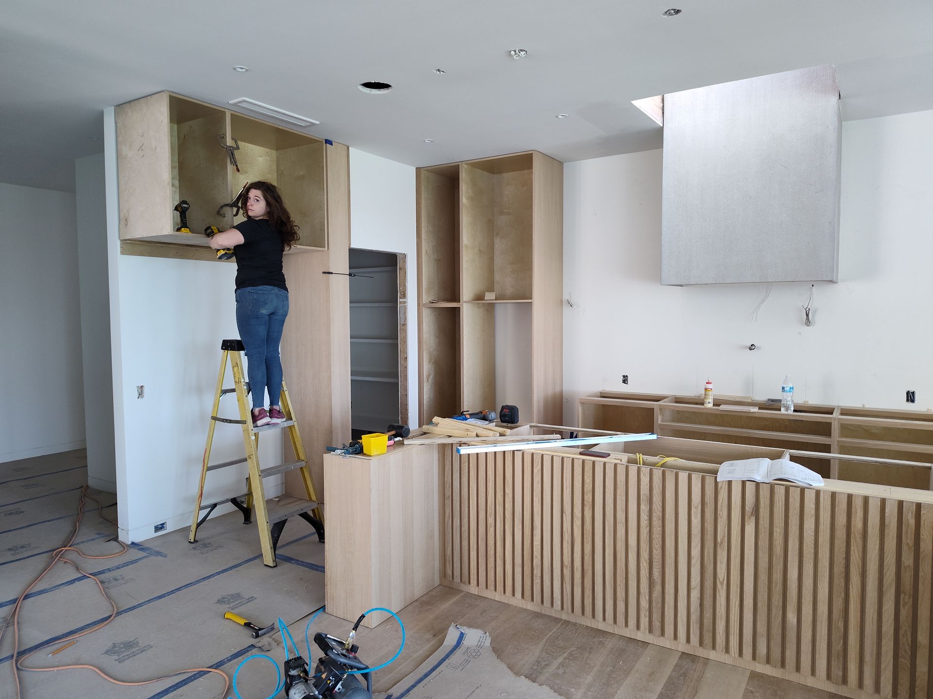 A woman is standing on a ladder in a kitchen.