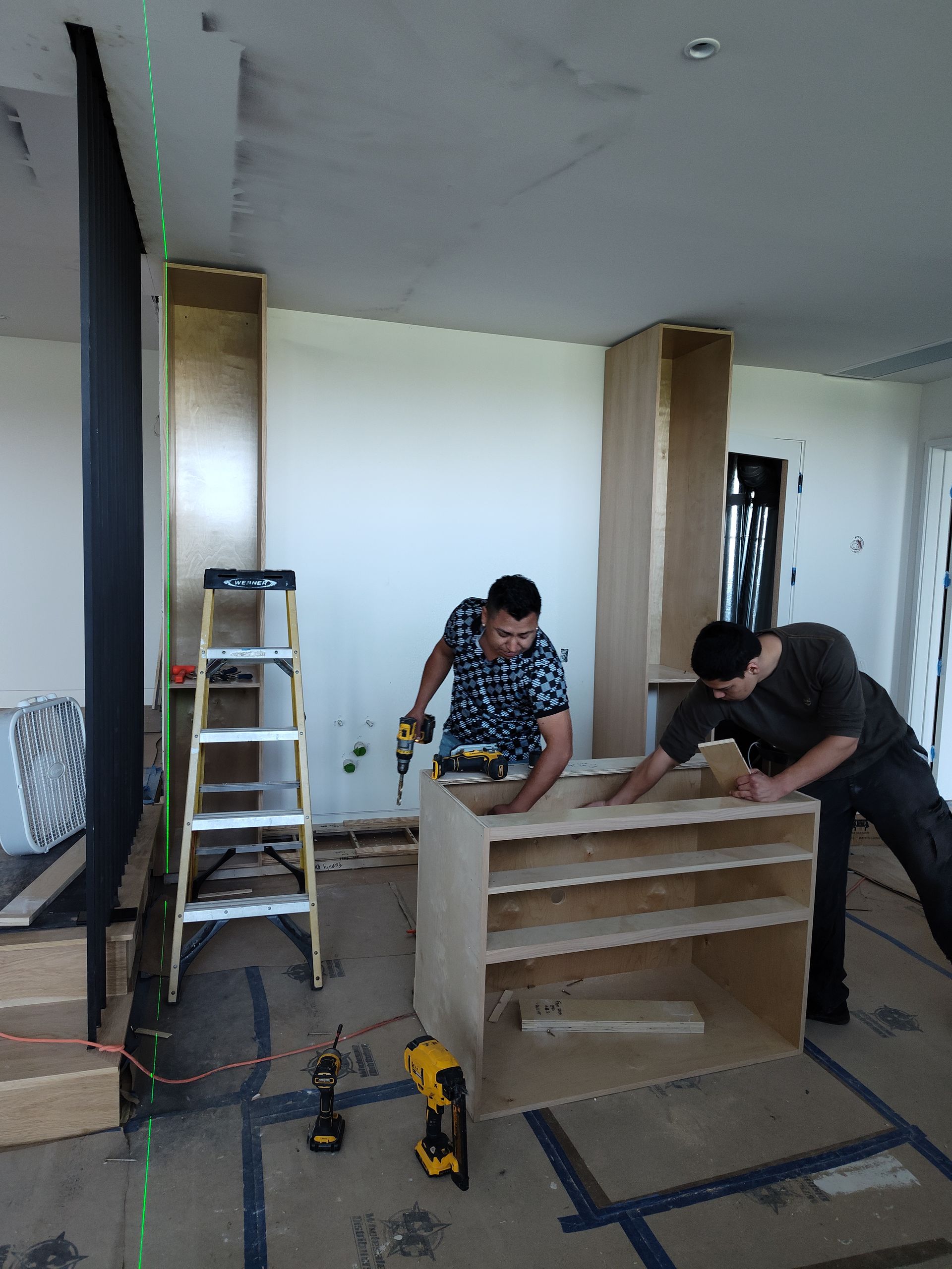 Two men are working on a piece of wood in a room.