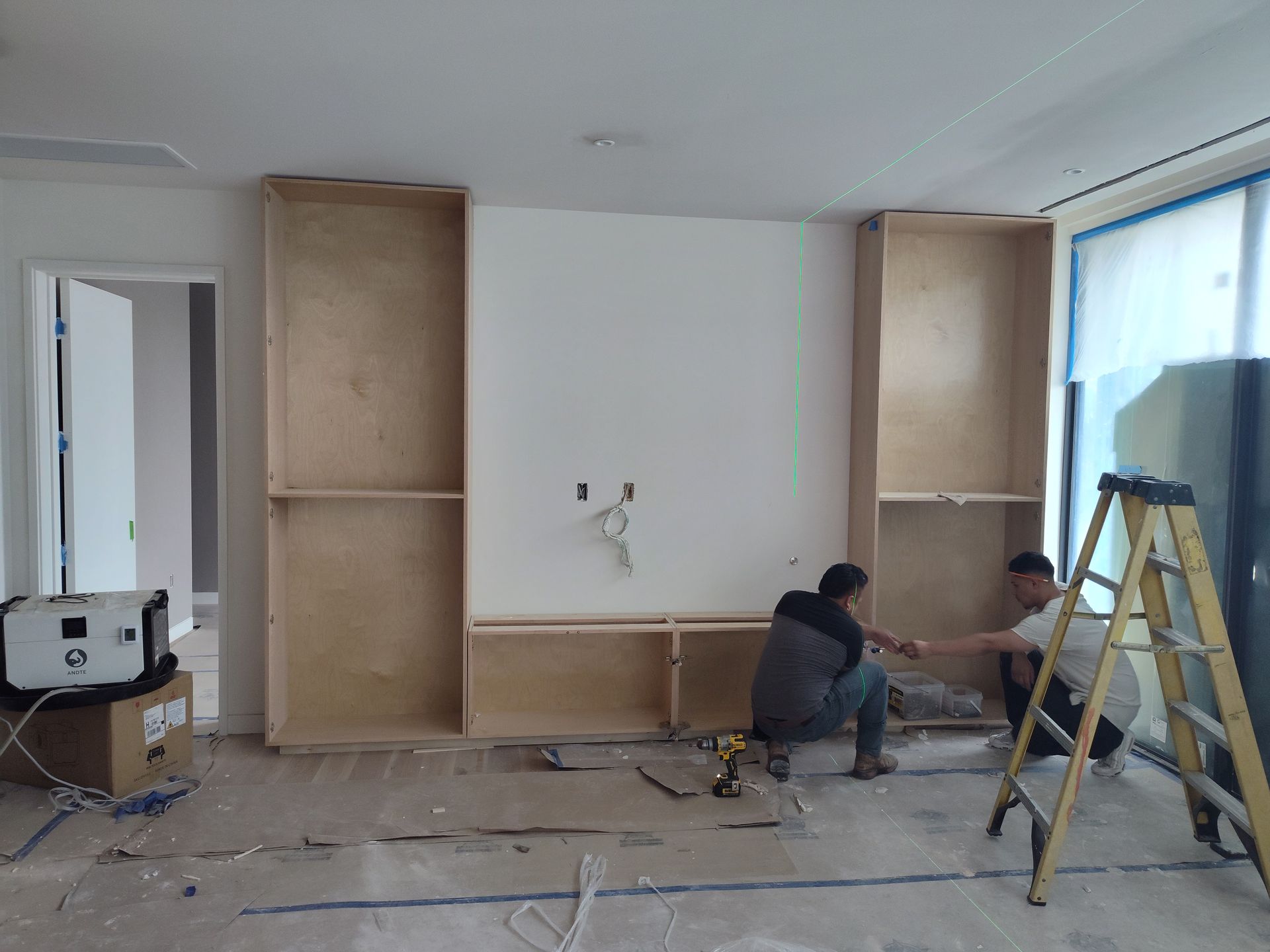 Two men are working on a shelf in a room with a ladder.