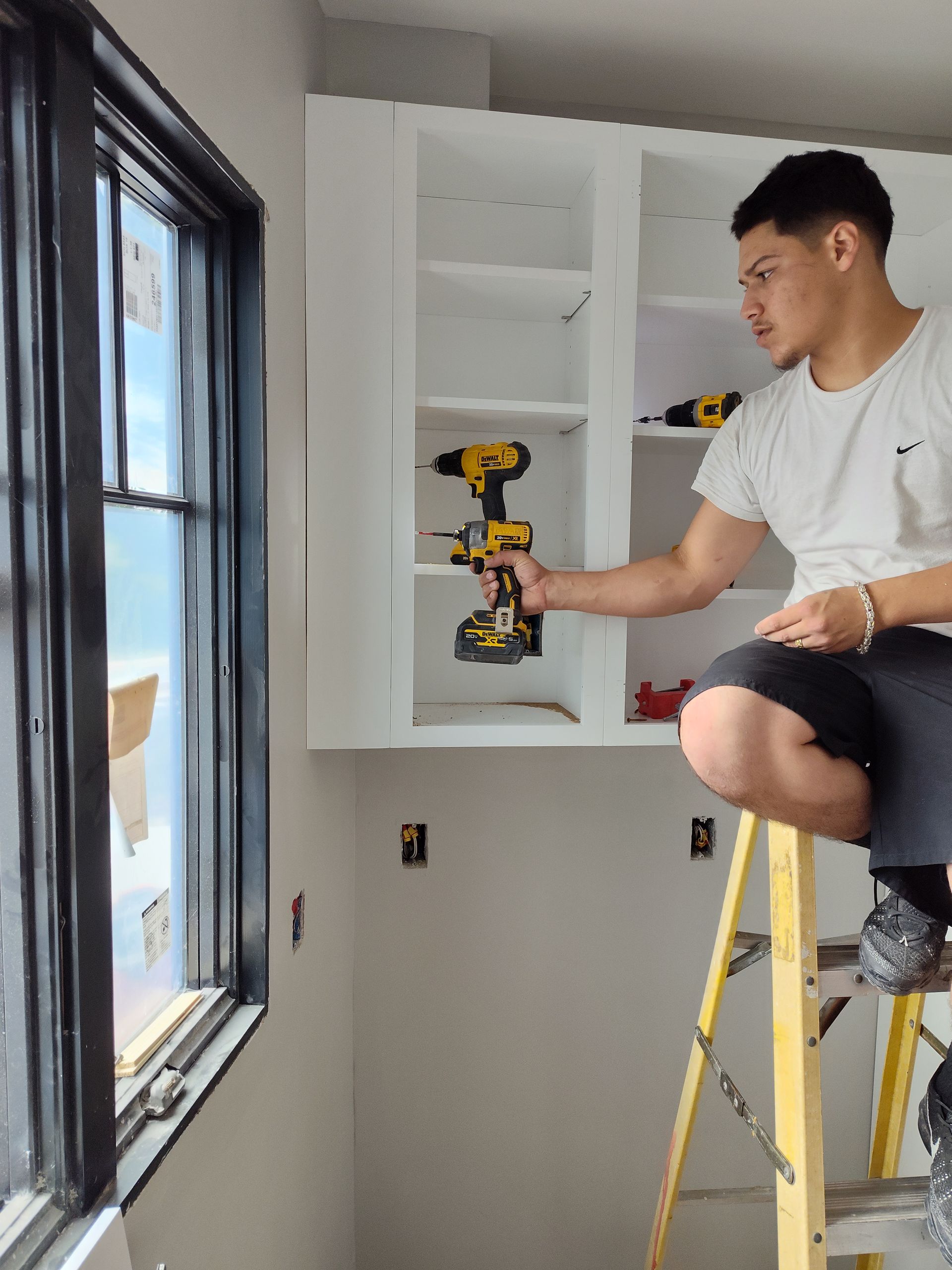 A man is sitting on a ladder holding a drill.