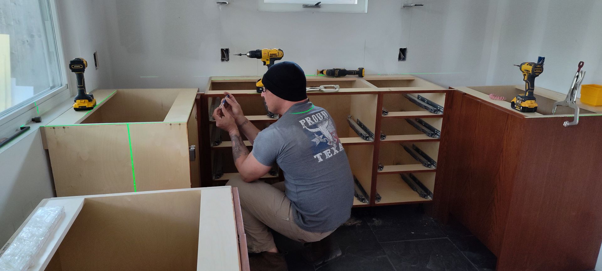 A man is kneeling down in a kitchen working on cabinets.
