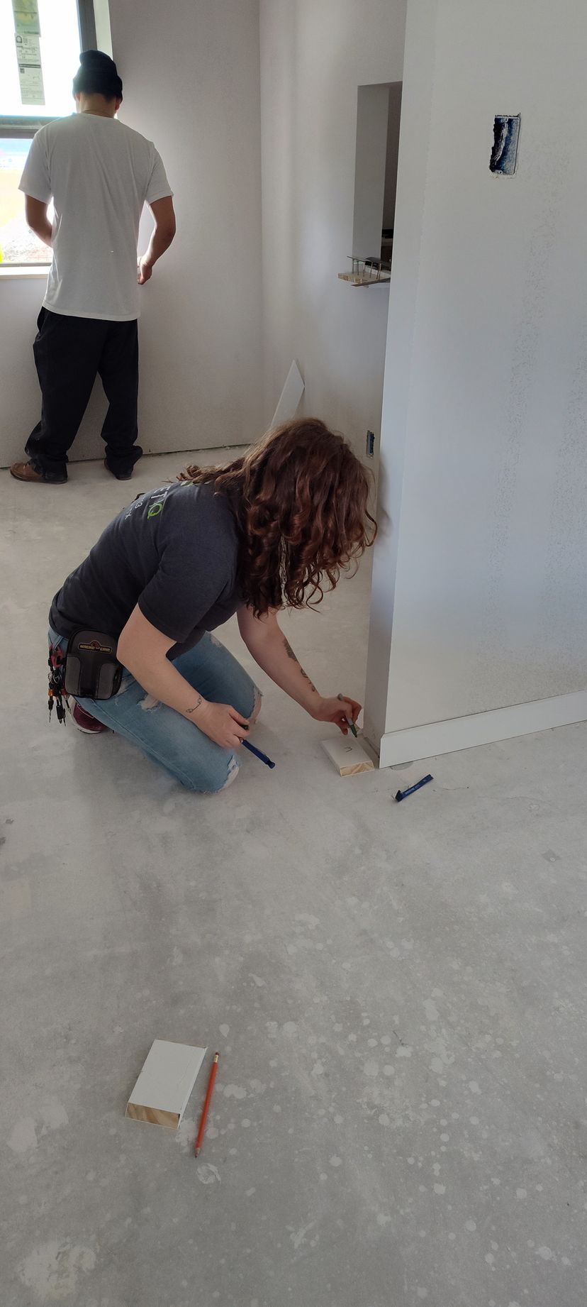 A man is kneeling on the floor while another man stands behind him.