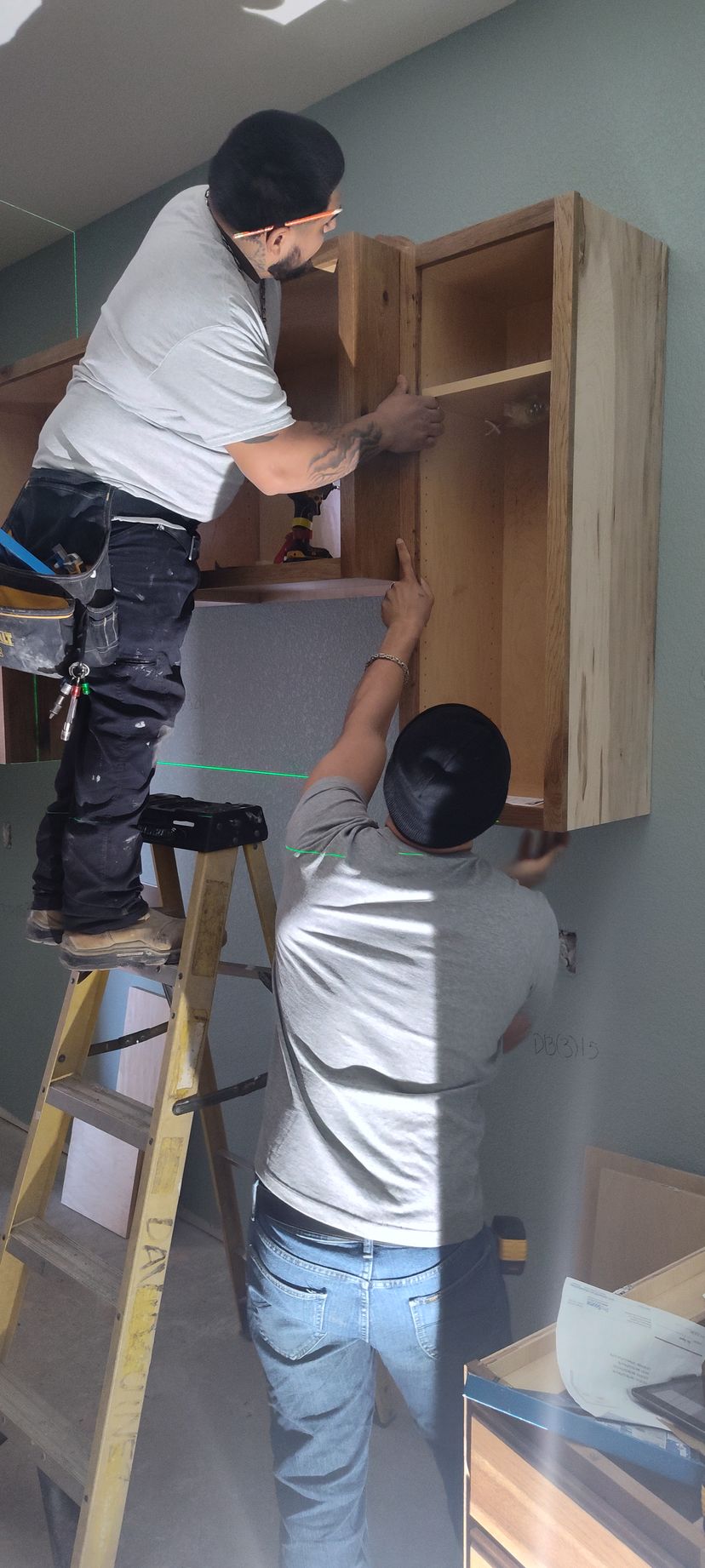 Two men are working on a cabinet in a kitchen.