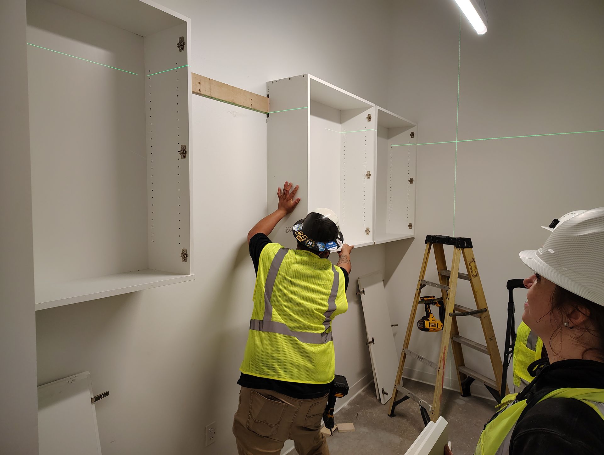A man and a woman are installing cabinets on a wall.