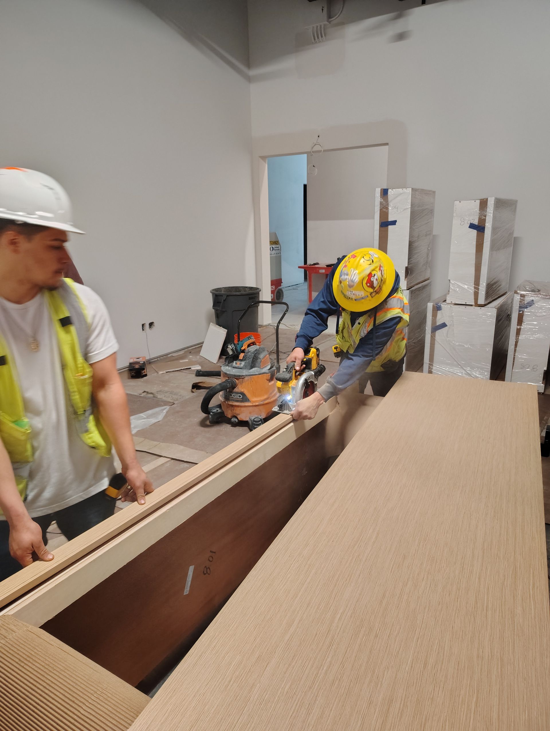 Two construction workers are working on a large piece of wood in a room.