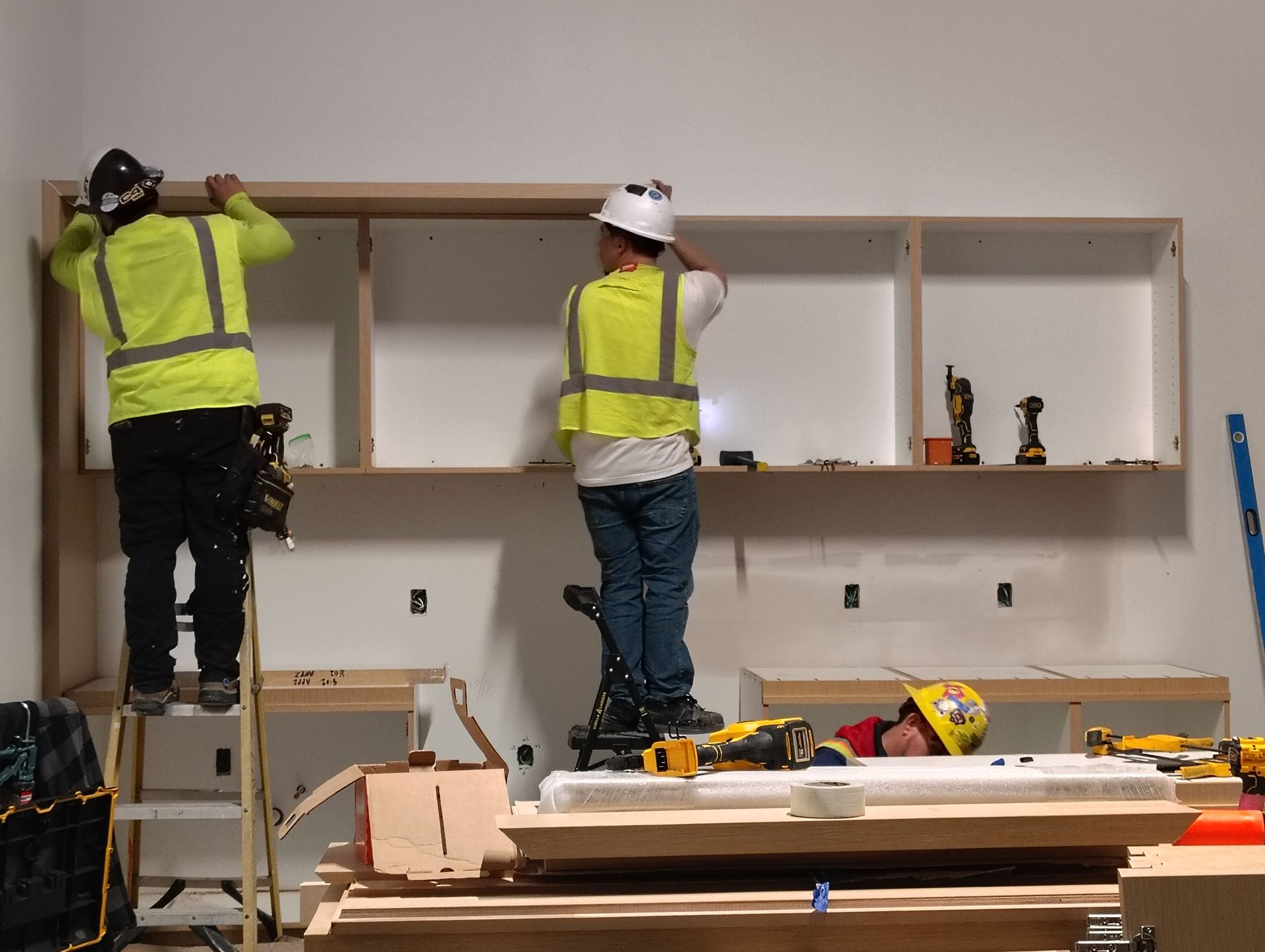 Two construction workers are working on a shelf in a room.