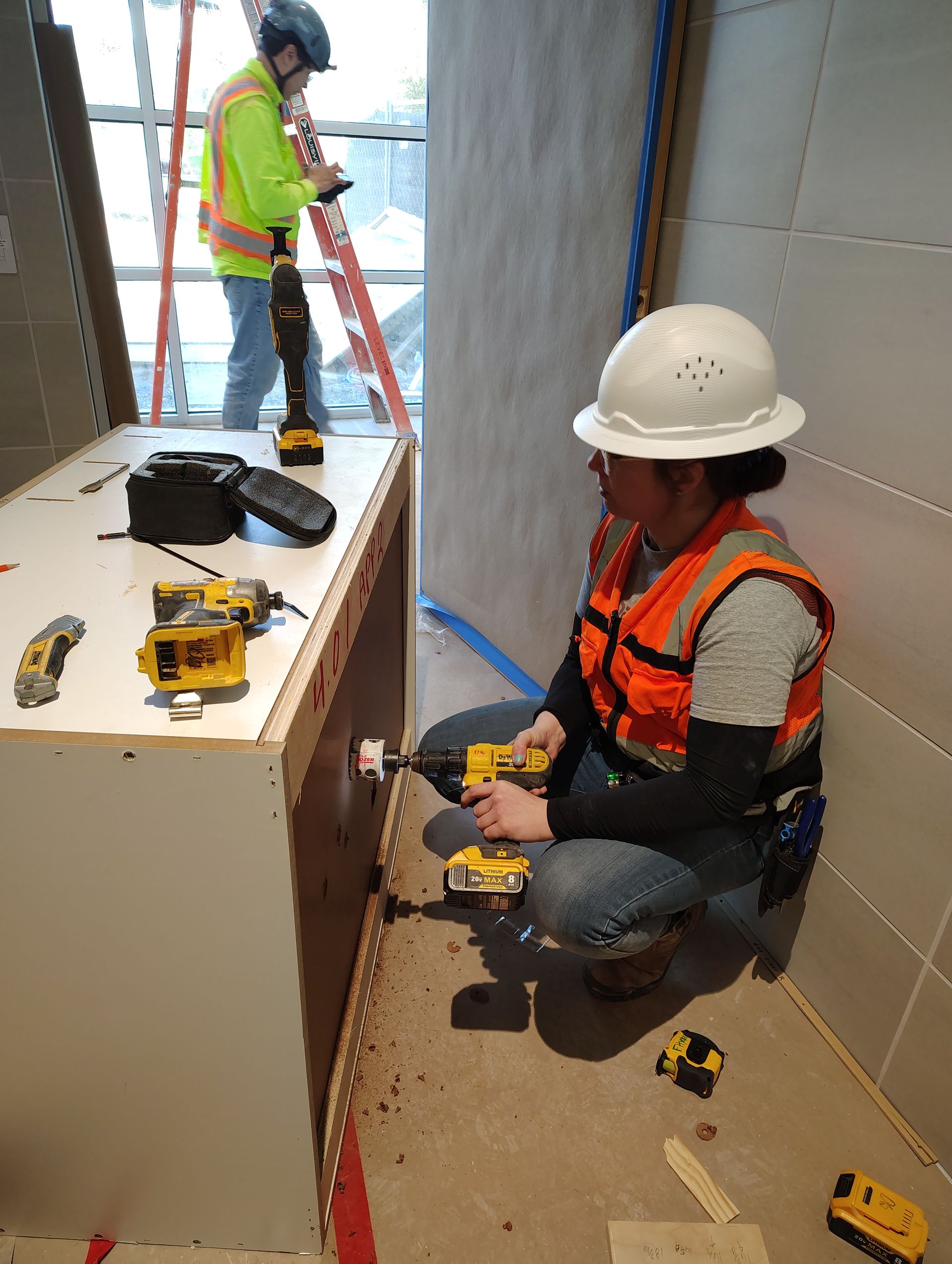 A woman is sitting on the floor working on a cabinet.