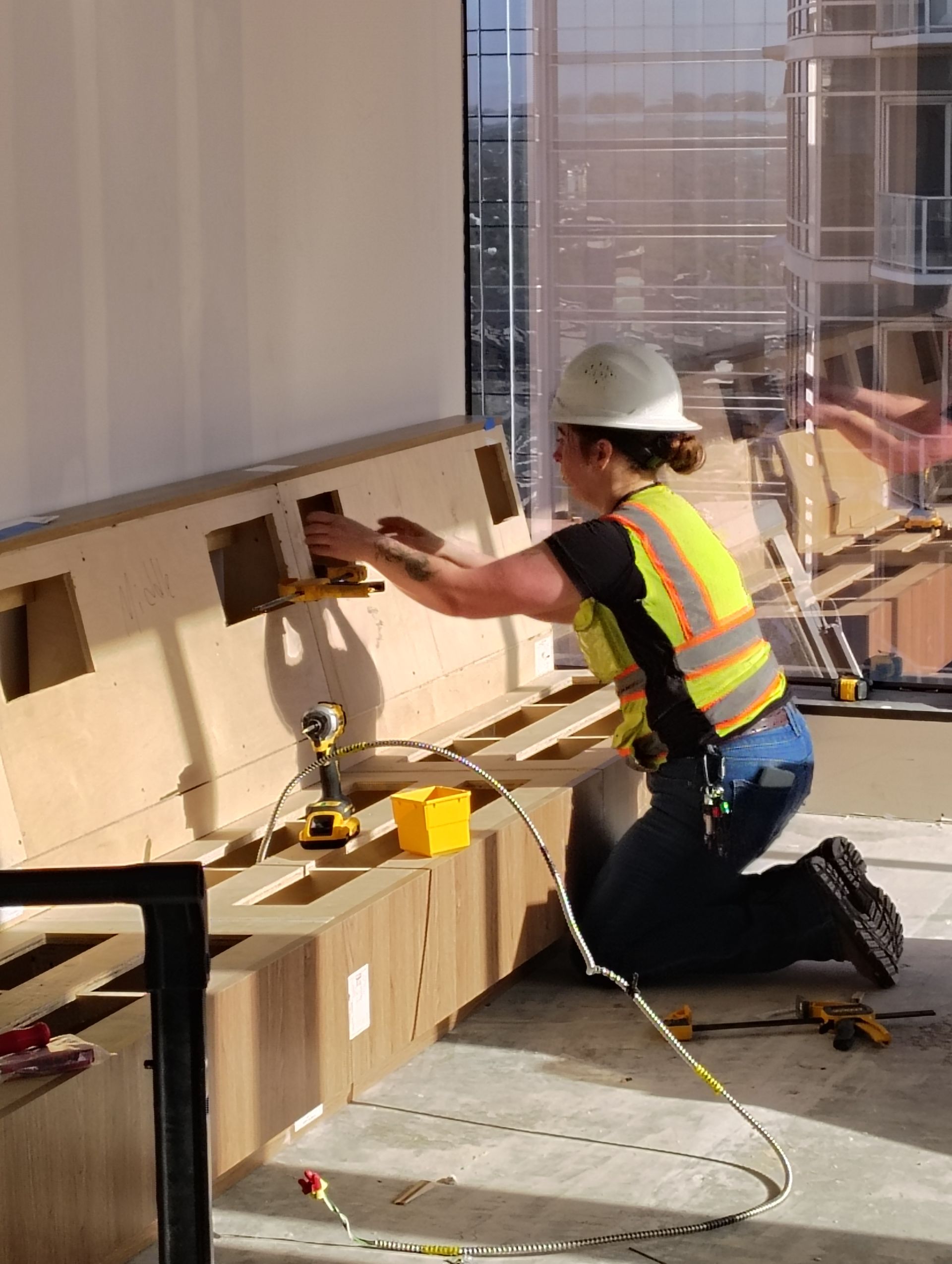 A woman wearing a hard hat and safety vest is working on a wall.
